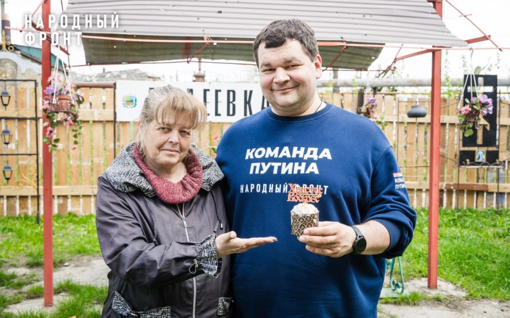 Жительница Авдеевки Людмила Николаевна вручает Сергею Самохину пасхальный кулич с самодельным топпером, который она разукрасила акриловыми красками